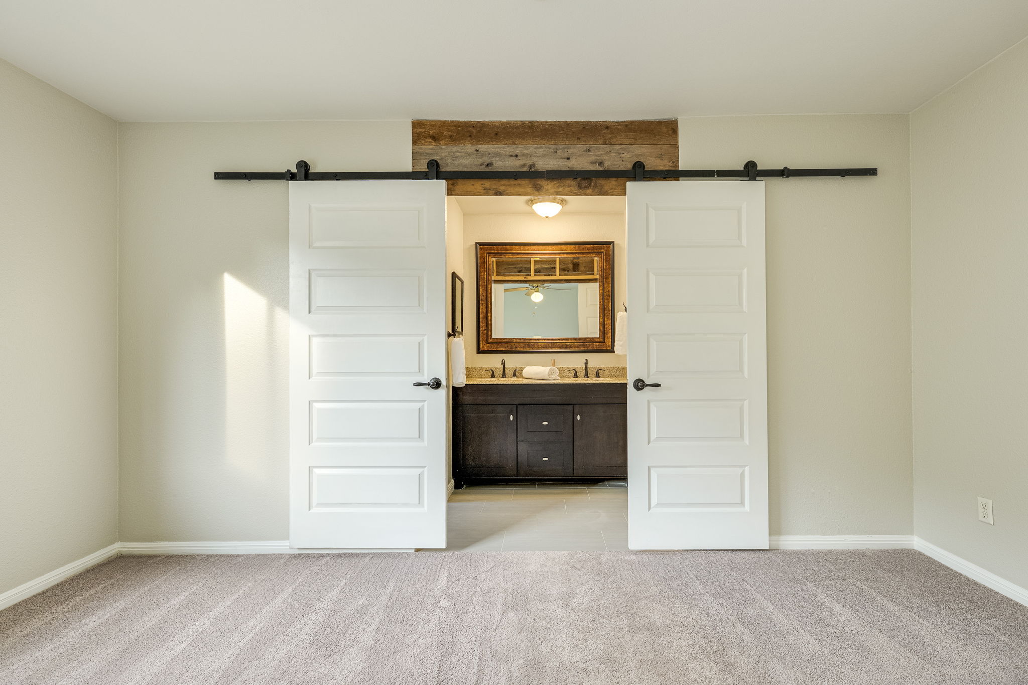 4815 Transit Circle Austin, TX 78727 - Photo 23 of 35 Barn door entry featuring a dual-sink vanity with dark wood cabinetry, a framed mirror, and a rustic wood accent beam