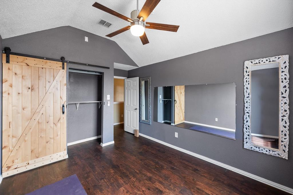 1305 Liverpool Lane Mansfield, TX 76063 - Photo 27 of 40 This room features dark wood-look flooring, a vaulted ceiling with a ceiling fan, and a barn door style closet