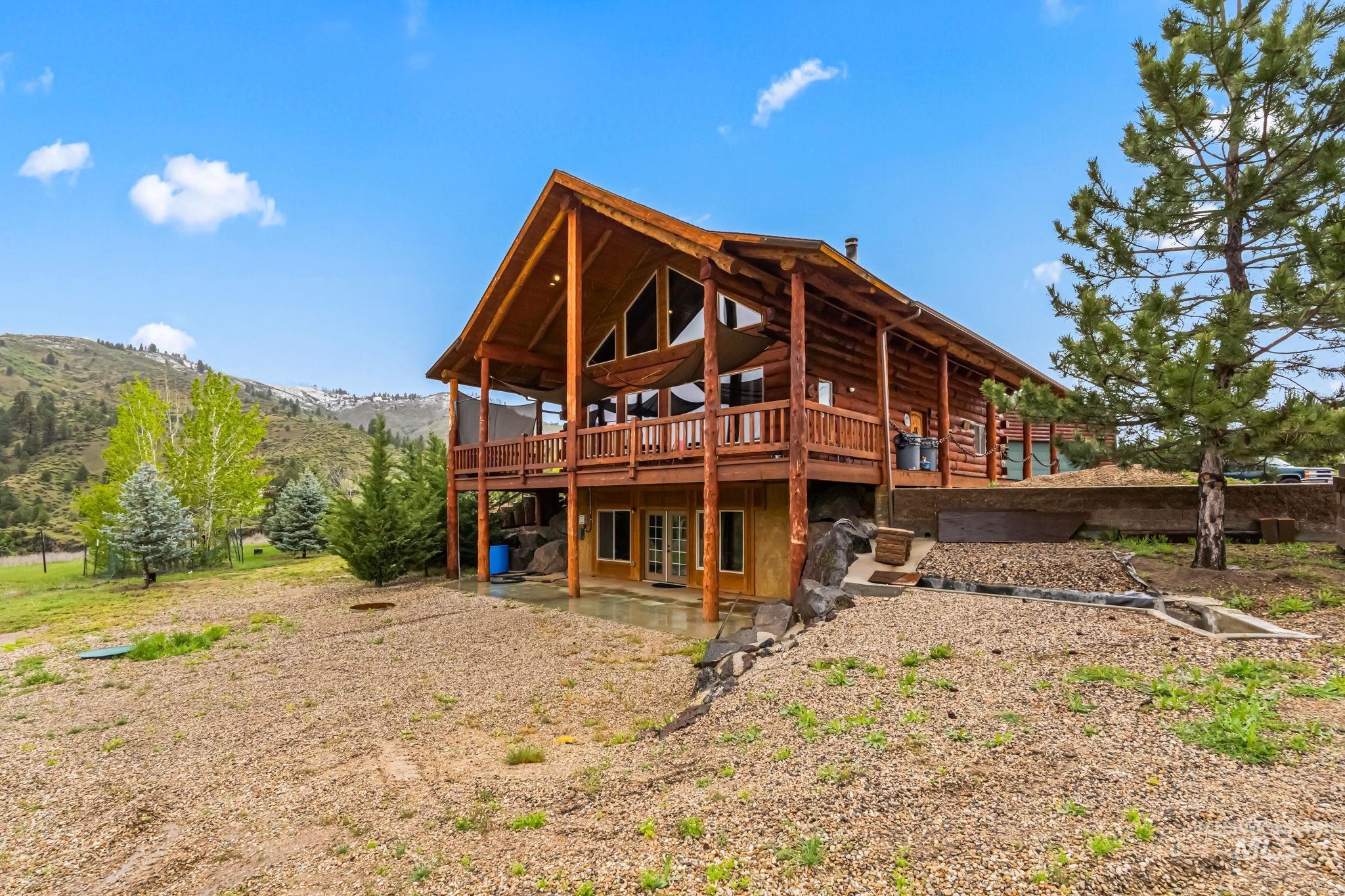 Rear view of property featuring log siding, a deck with mountain view, and a patio