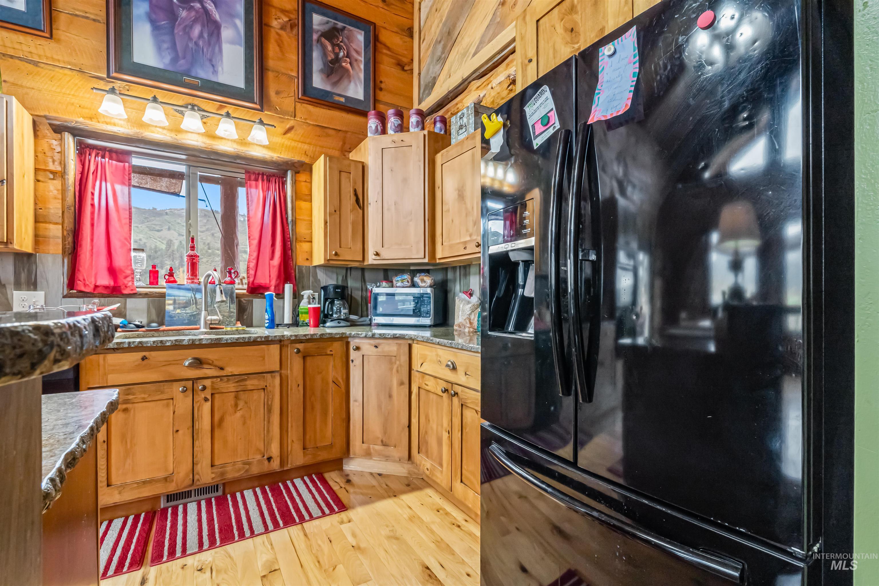 15 Rim Canyon Lane Boise, ID 83716 - Photo 11 of 31 Kitchen featuring black refrigerator with ice dispenser, light wood-style flooring, wood finish cabinets, dark stone countertops, and stainless steel microwave