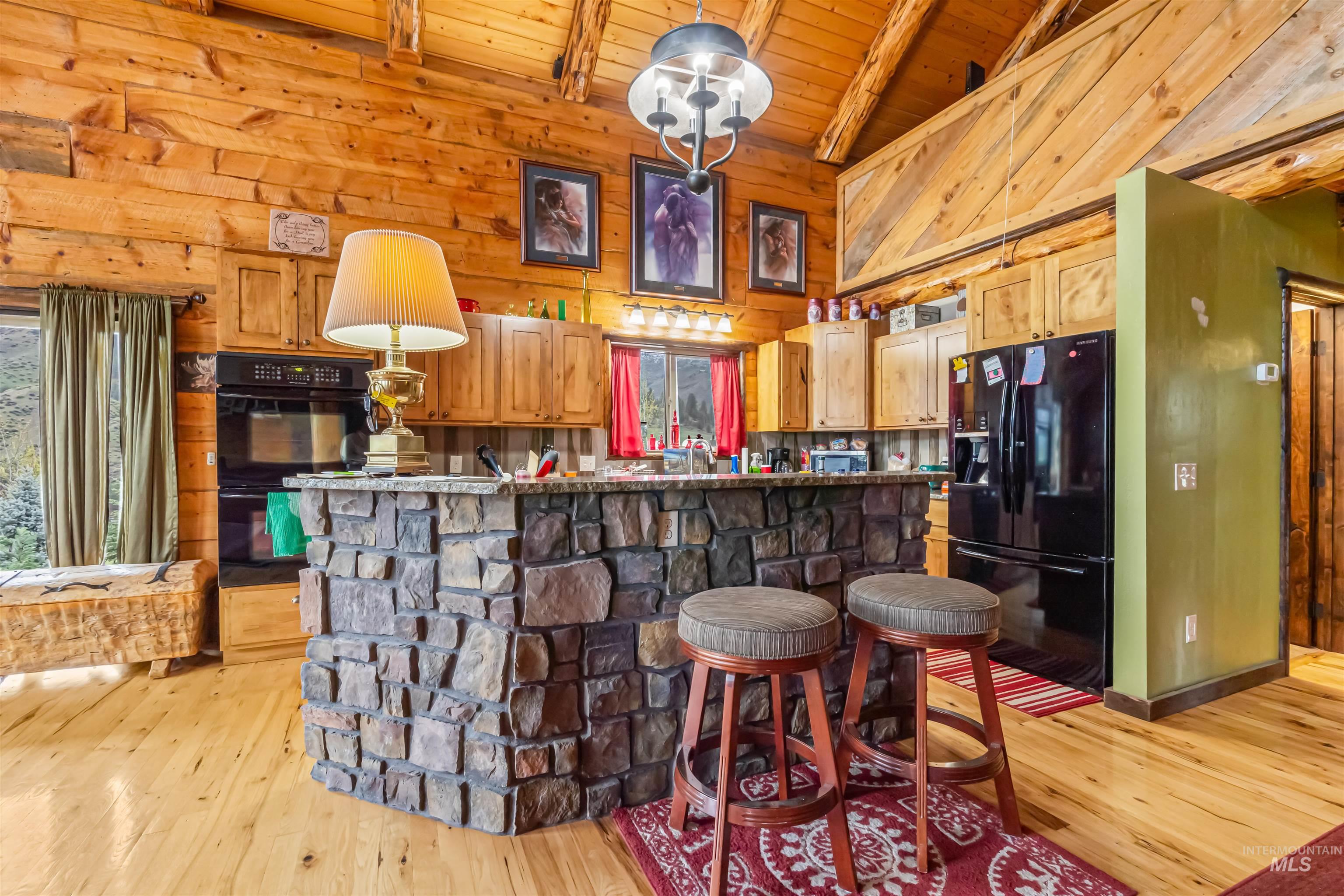 15 Rim Canyon Lane Boise, ID 83716 - Photo 12 of 31 Kitchen featuring black appliances, wooden walls, a high wood beamed ceiling, a breakfast bar area, and light wood-style floors