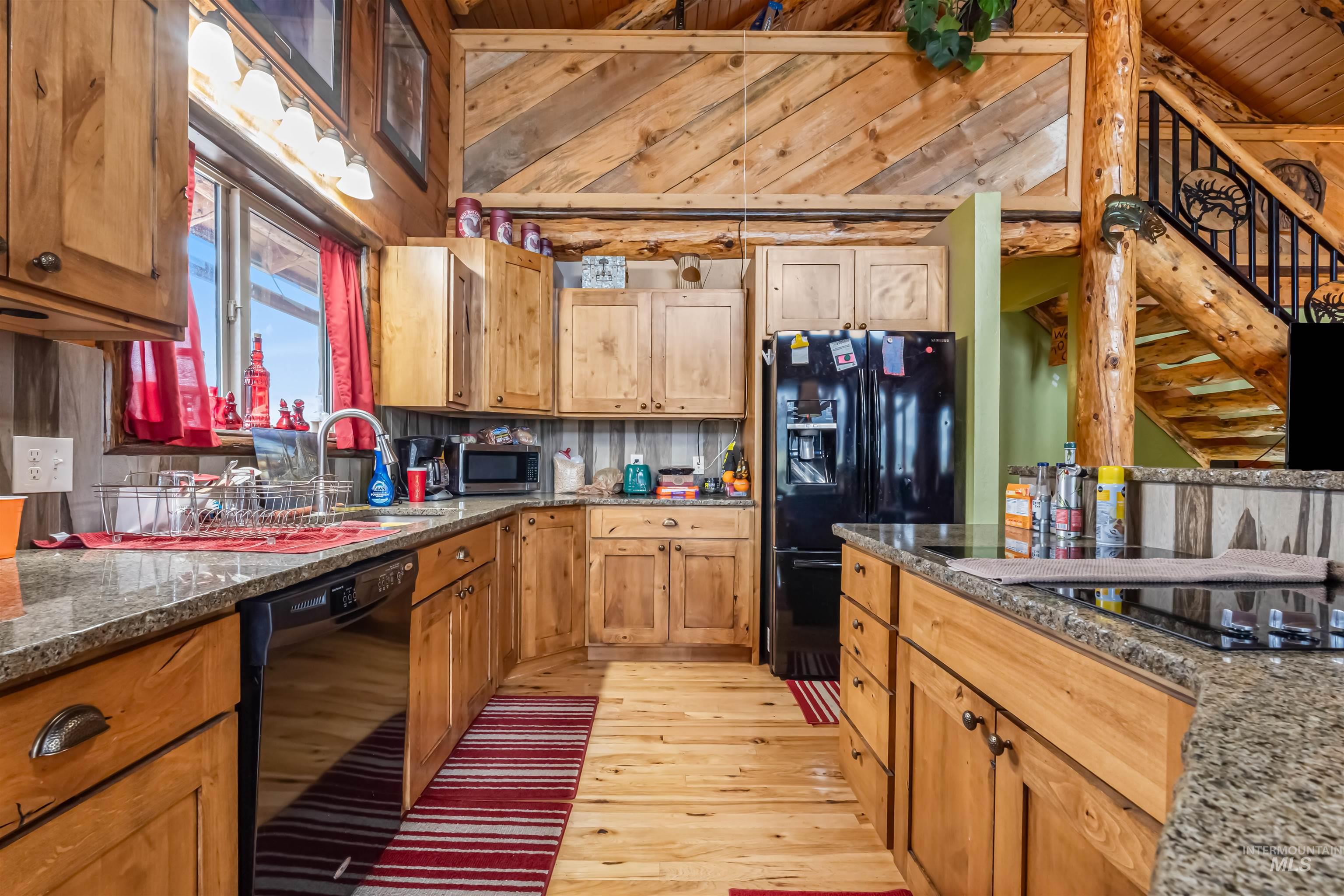 15 Rim Canyon Lane Boise, ID 83716 - Photo 10 of 31 Kitchen featuring black appliances, light wood-style floors, dark stone countertops, wood finish cabinets, and a vaulted wood ceiling