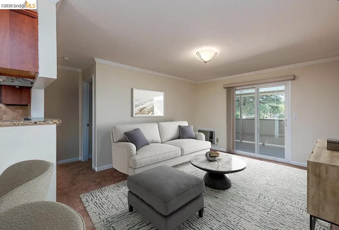 1505 Kirker Pass Road, Unit 214 Concord, CA 94521 - Photo 9 of 55 Living area featuring a sliding glass door to an outdoor patio, crown molding, and a built-in kitchen pass-through with a granite countertop and wood cabinetry