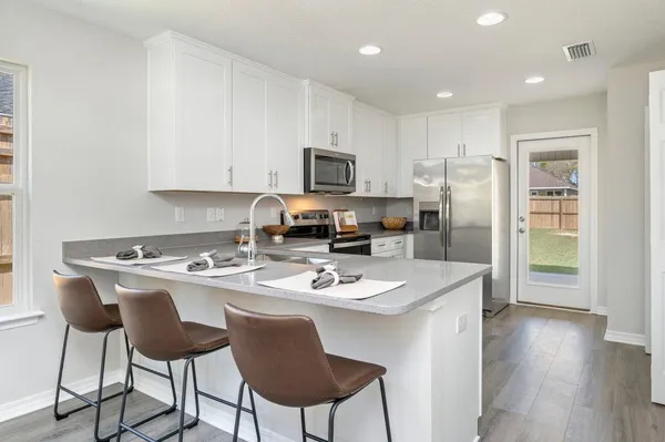 a kitchen with stainless steel appliances granite countertop a refrigerator a stove a sink a dining table and chairs with wooden floor