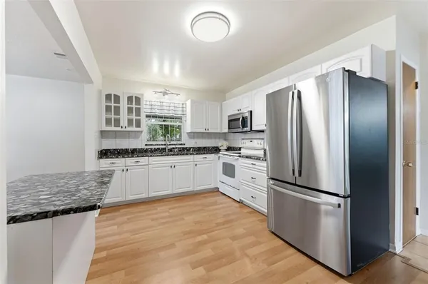 a kitchen with granite countertop a refrigerator oven a sink and white cabinets