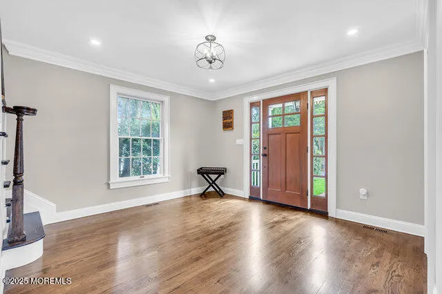 an empty room with wooden floor chandelier and windows