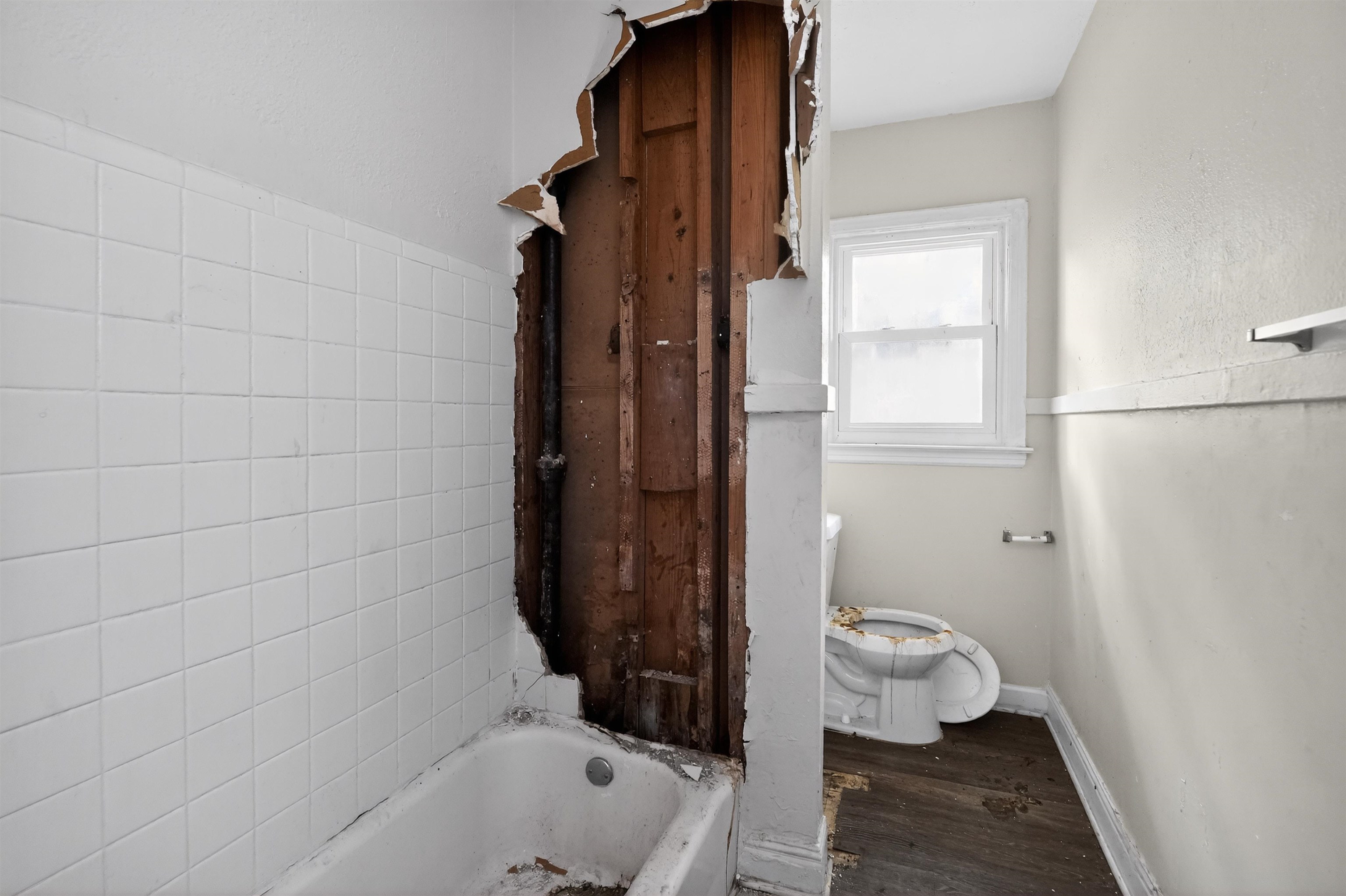 949 Sumter Street Memphis, TN 38122 - Photo 29 of 33 Bathroom space featuring white square wall tiles, a white bathtub, a single pane window, and wood-finish flooring