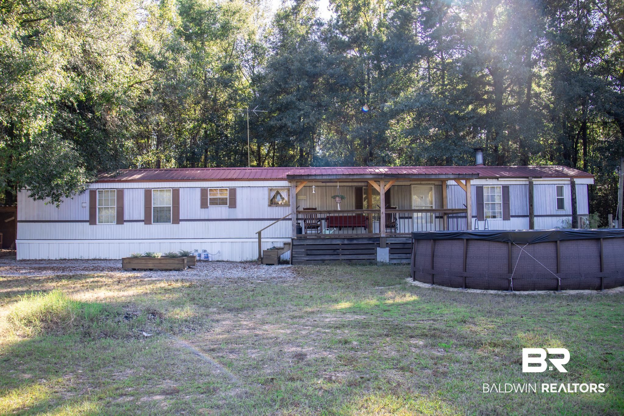 588 A D Clark Road Castleberry, AL 36432 - Photo 1 of 17 Manufactured / mobile home featuring a covered pool, covered porch, a front yard, view of wooded area, and a metal roof