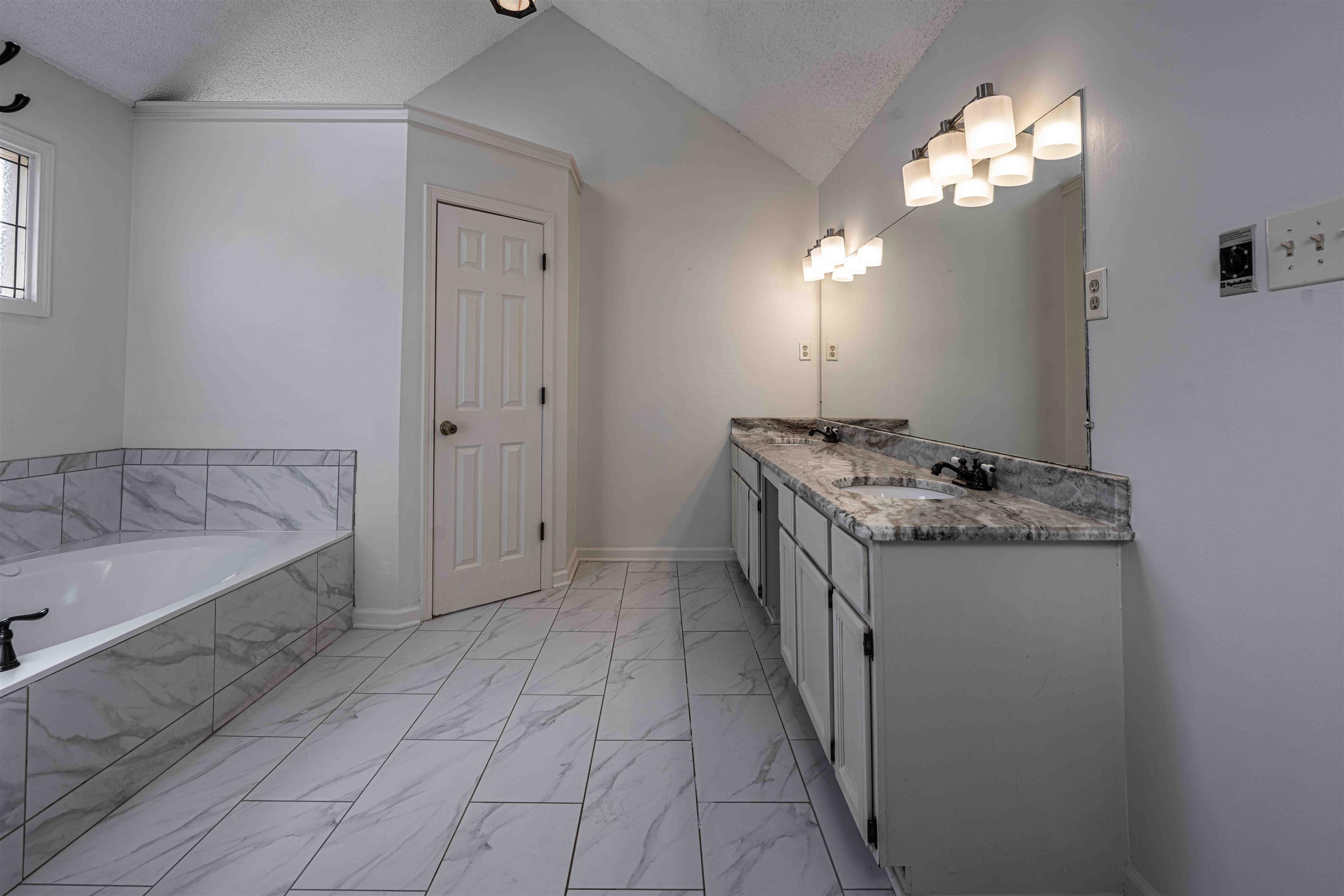 8883 Farmoor Road Germantown, TN 38139 - Photo 22 of 34 Full bathroom with double vanity, vaulted ceiling, light marble finish floors, a bath, and a textured ceiling