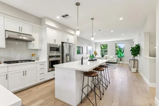 a kitchen with stainless steel appliances kitchen island granite countertop a stove a sink a refrigerator and white cabinets with wooden floor