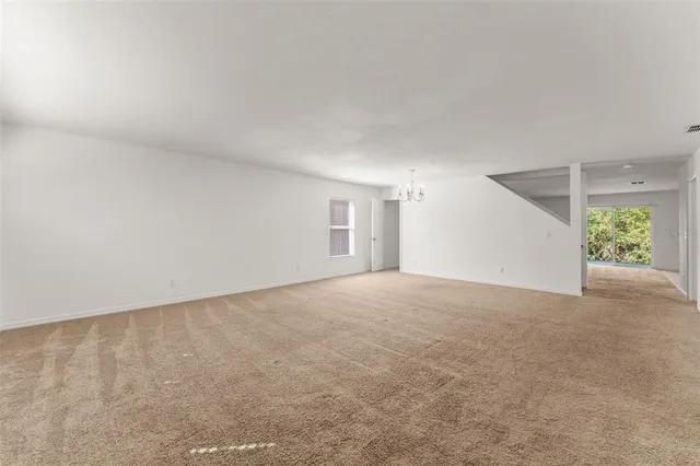 an empty room with chandelier fan and windows