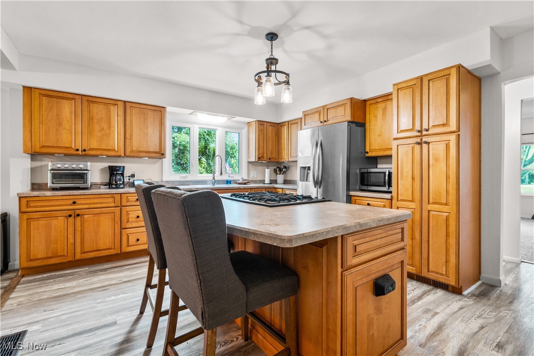 6170 Oberlin Road Amherst, OH 44001 - Photo 22 of 39 Kitchen with appliances with stainless steel finishes, a center island, brown cabinets, a kitchen breakfast bar, and light wood-style flooring