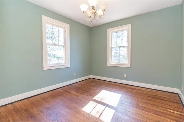 an empty room with wooden floor chandelier and windows