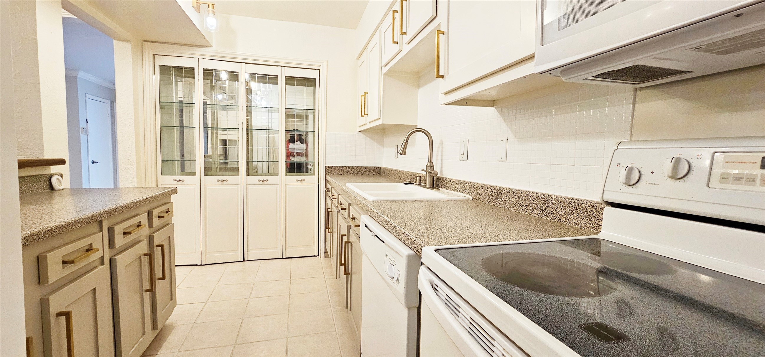 11550 Chimney Rock Road, Unit 205 Houston, TX 77035 - Photo 13 of 27 Updated kitchen featuring white cabinetry with gold hardware, granite-look countertops, and ample storage including glass-front pantry doors. Includes all appliances—microwave, stove, dishwasher, and refrigerator.