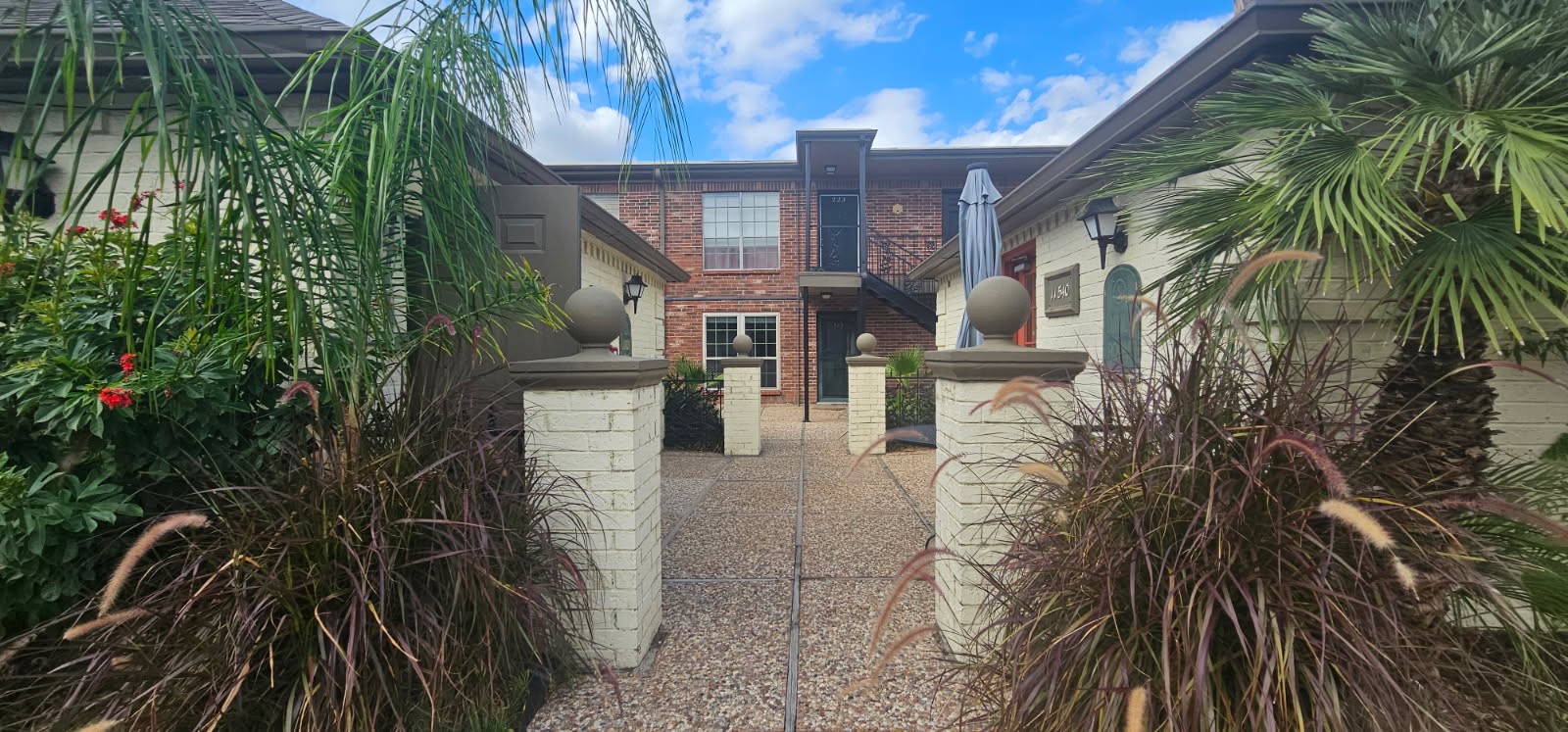 11550 Chimney Rock Road, Unit 205 Houston, TX 77035 - Photo 22 of 27 Beautifully landscaped courtyard surrounded by palm trees and flowering plants, creating a relaxing outdoor setting.