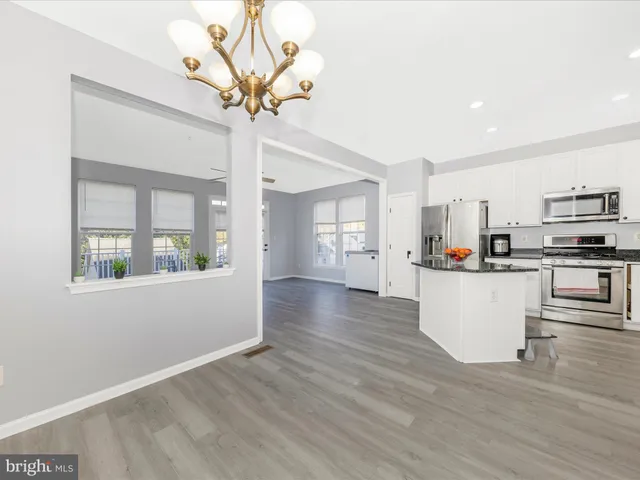 a living room with stainless steel appliances kitchen island granite countertop a refrigerator a stove top oven a sink and white cabinets with wooden floor