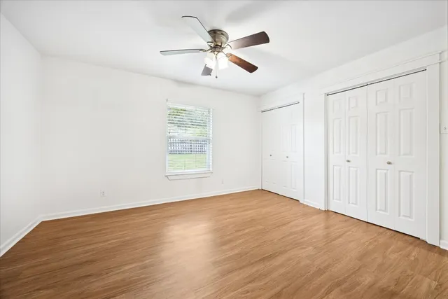 an empty room with wooden floor ceiling fan and windows