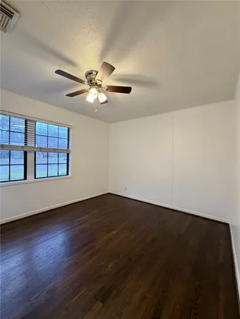 a view of an empty room with wooden floor and a ceiling fan