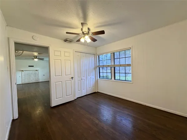 an empty room with wooden floor chandelier fan and windows
