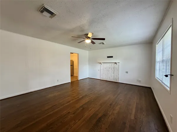 an empty room with wooden floor chandelier fan and windows