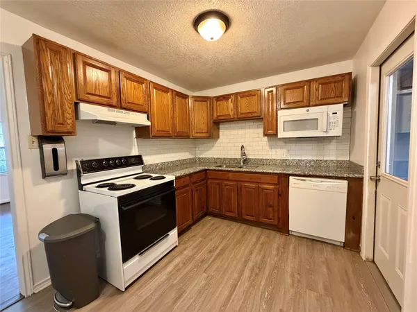 a kitchen with granite countertop wooden floors and white stainless steel appliances