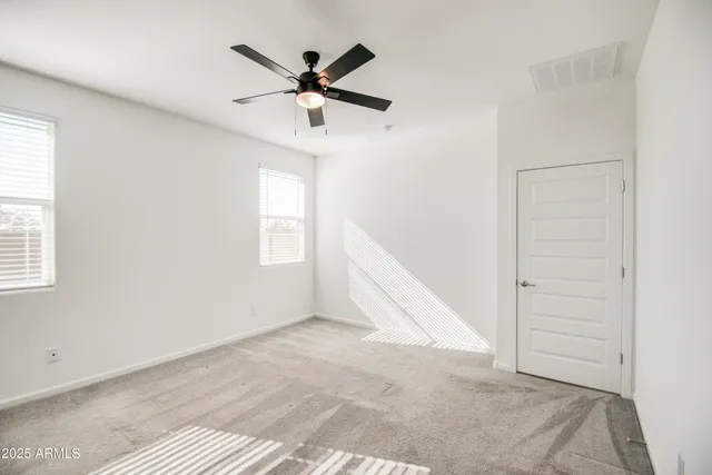 an empty room with ceiling fan and windows
