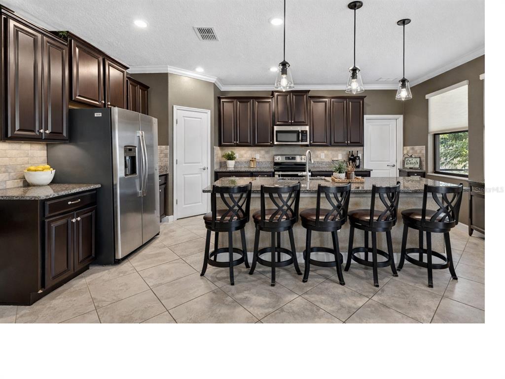 9906 Victory Gallop Loop Ruskin, FL 33573 - Photo 5 of 18 a kitchen with stainless steel appliances kitchen island granite countertop a table chairs and a refrigerator