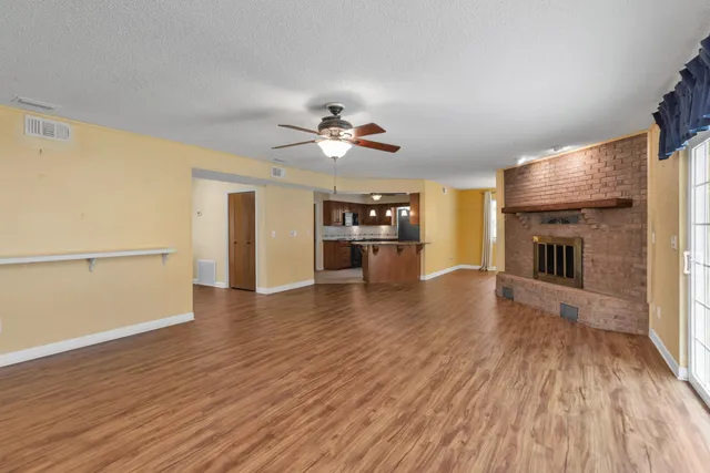 an empty room with wooden floor fireplace and a kitchen space