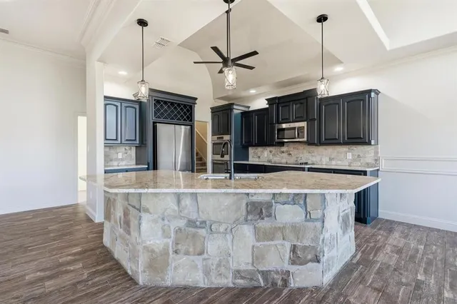 a view of a kitchen with kitchen island a large counter top space stainless steel appliances and wooden floor