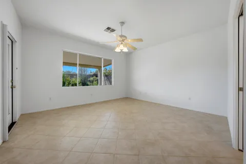 an empty room with chandelier fan and windows