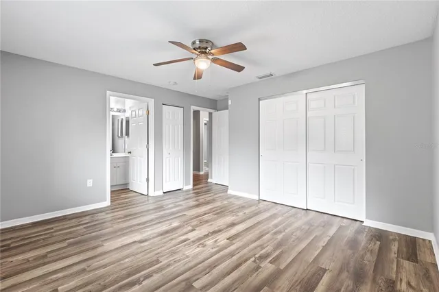 a view of an empty room with wooden floor and a ceiling fan