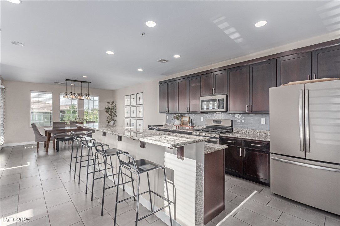 3165 Via Como Henderson, NV 89044 - Photo 6 of 42 Kitchen with stainless steel appliances, backsplash, dark brown cabinets, a breakfast bar area, and recessed lighting