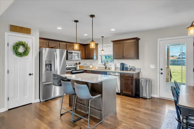 a kitchen with stainless steel appliances granite countertop a refrigerator a stove a sink a island and chairs with wooden floor