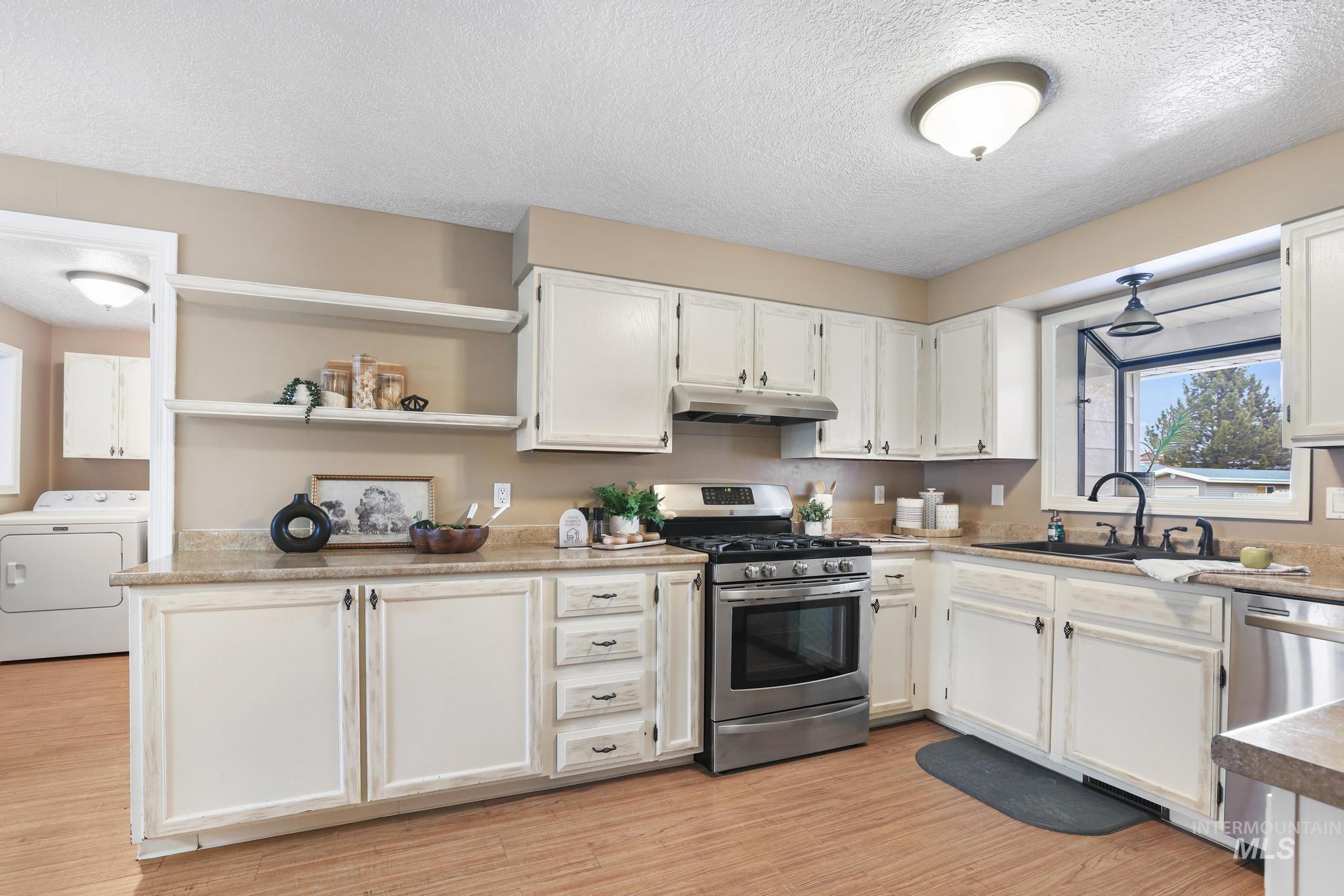 1143 Starfire Street Twin Falls, ID 83301 - Photo 8 of 32 Kitchen with open shelves, white cabinetry, stainless steel appliances, washer / clothes dryer, and a textured ceiling