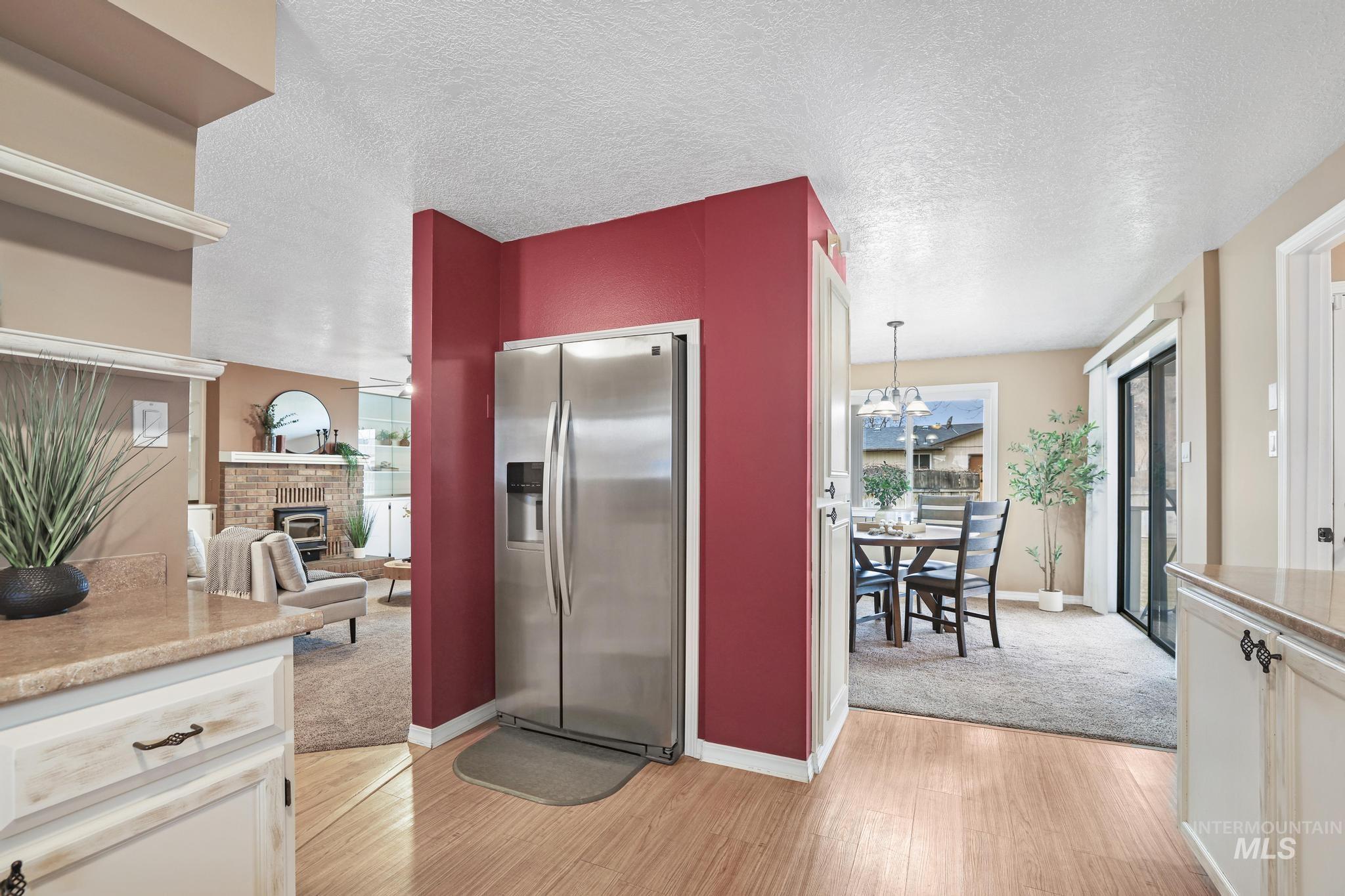 1143 Starfire Street Twin Falls, ID 83301 - Photo 9 of 32 Kitchen with stainless steel fridge, a glass covered fireplace, light wood-style floors, a textured ceiling, and hanging light fixtures