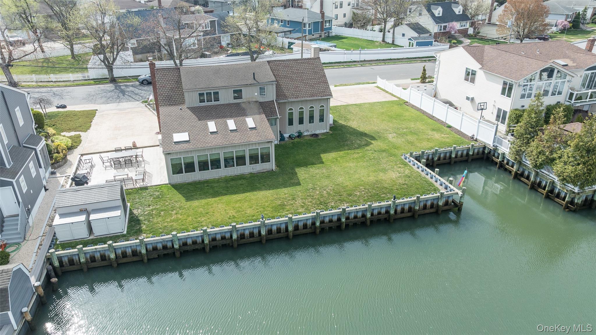 3414 Riverside Drive Oceanside, NY 11572 - Photo 21 of 25 Waterfront property featuring a well-maintained bulkhead, a sunroom with multiple skylights, a patio area, and a paved driveway