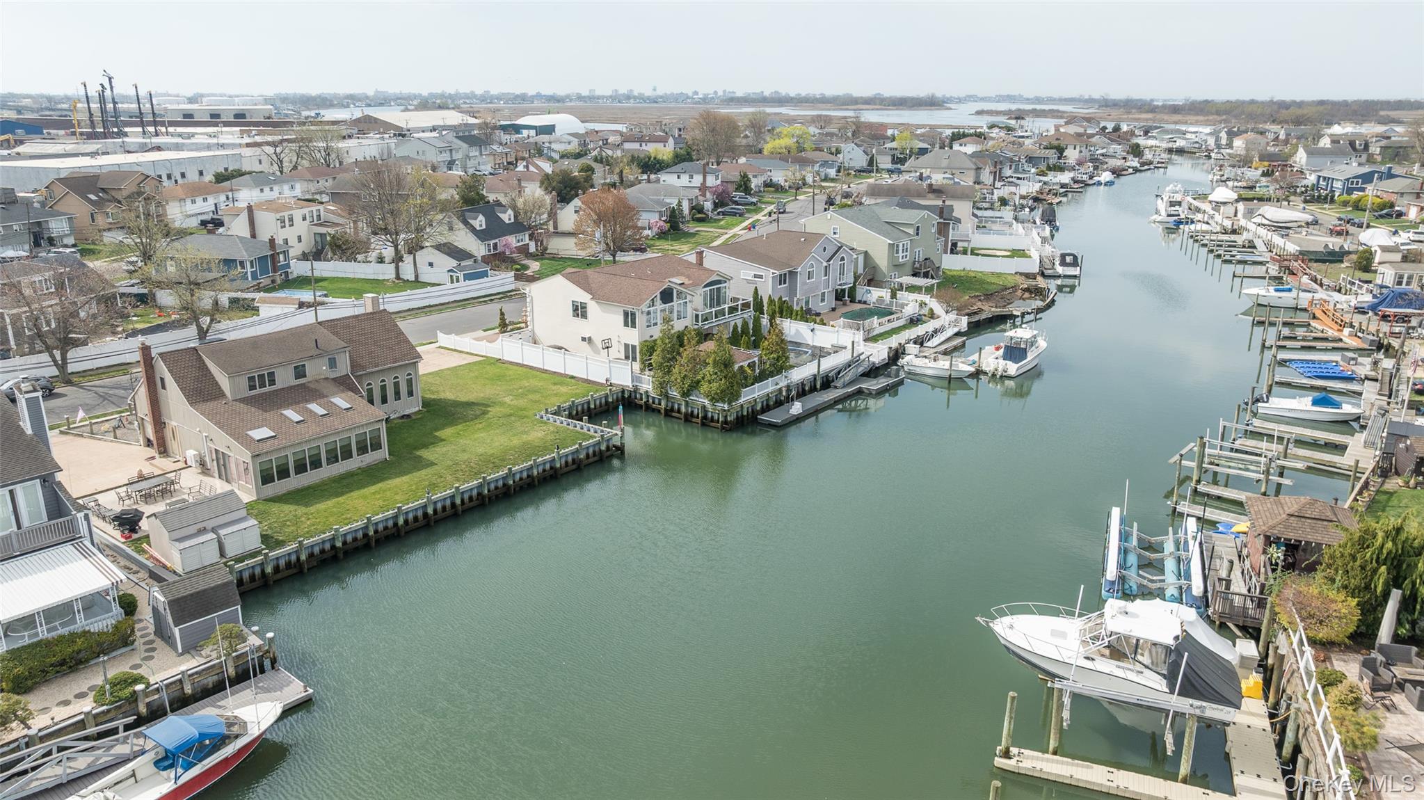 3414 Riverside Drive Oceanside, NY 11572 - Photo 22 of 25 Waterfront property featuring a private boat dock, expansive backyard, sunroom with multiple skylights, and a two-story residence with a prominent chimney