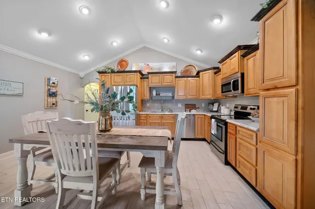 a kitchen with stainless steel appliances granite countertop a stove top oven a refrigerator a sink and a dining table with white cabinets