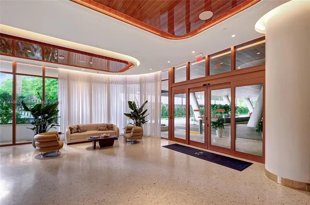 a living room with furniture two large window and wooden floor