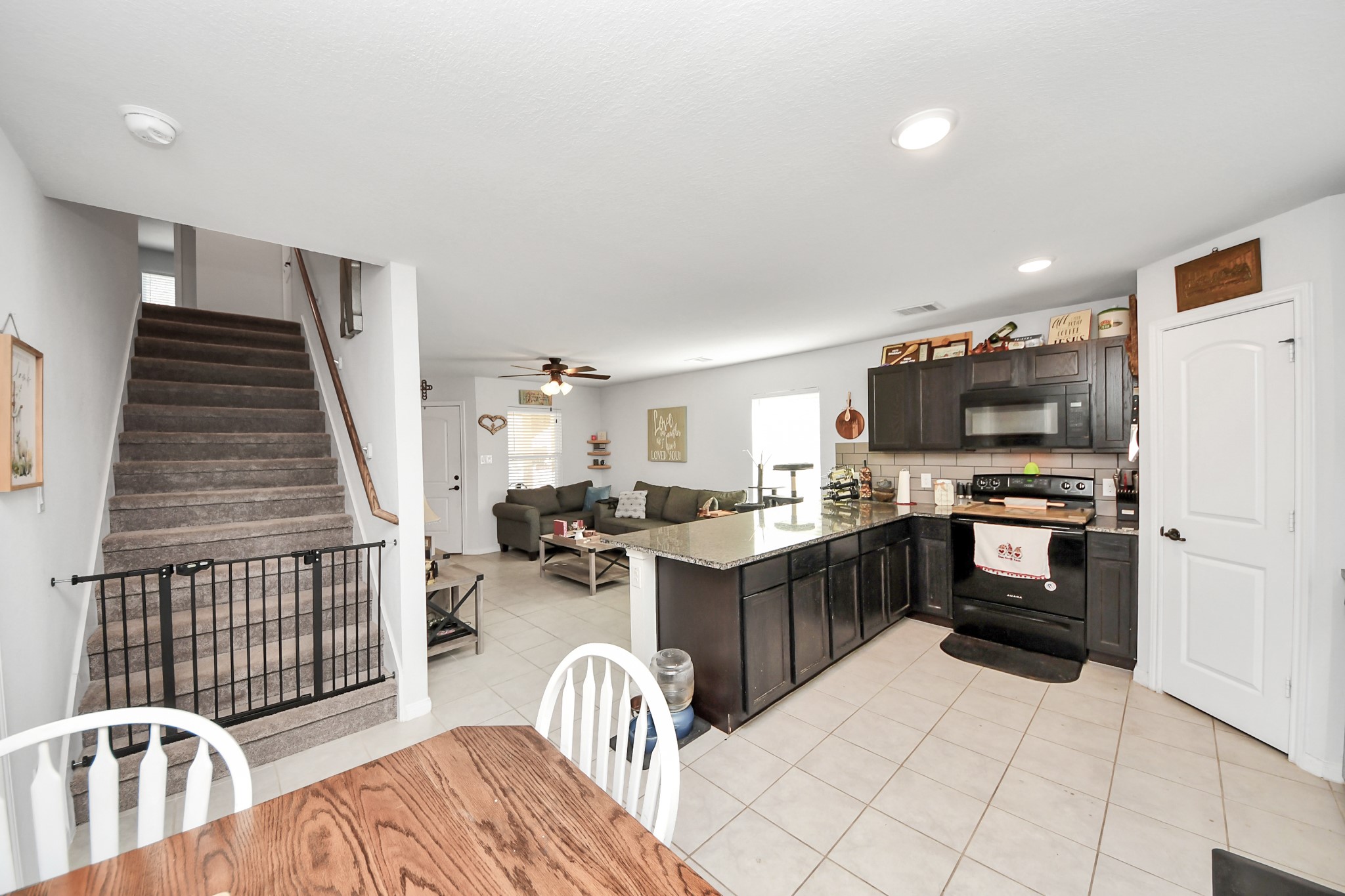 15291 Arrowhead Loop West Willis, TX 77378 - Photo 13 of 28 This inviting home features an open-concept living area with a modern kitchen, complete with dark cabinetry and granite countertops. The adjacent dining space and cozy living room are perfect for entertaining. A carpeted staircase leads to the upper level, adding to the home's functional layout.