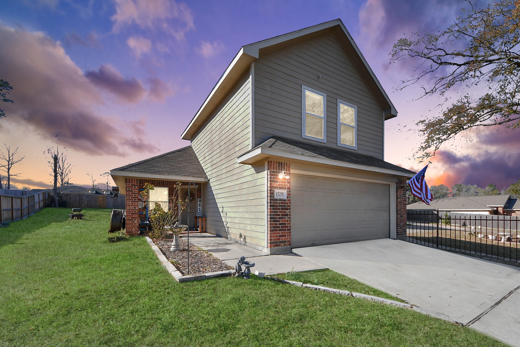 15291 Arrowhead Loop West Willis, TX 77378 - Photo 2 of 28 This photo showcases a two-story house with a modern exterior, featuring a combination of brick and siding. The property includes a spacious driveway, a well-maintained lawn, and a fenced backyard. The setting sun adds a warm glow, enhancing the home's inviting appearance.