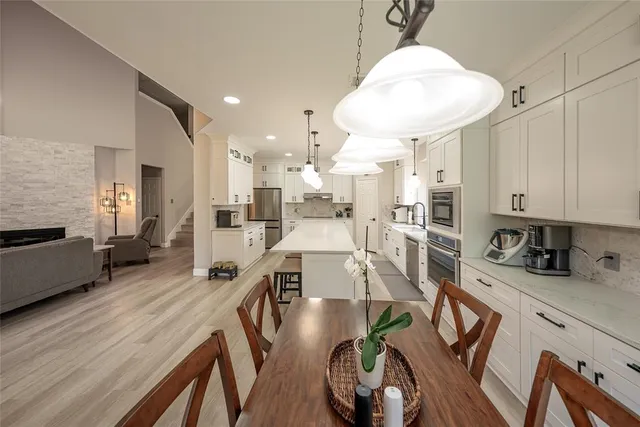 a kitchen with stainless steel appliances kitchen island granite countertop a stove a refrigerator a oven a sink a dining table and chairs with wooden floor