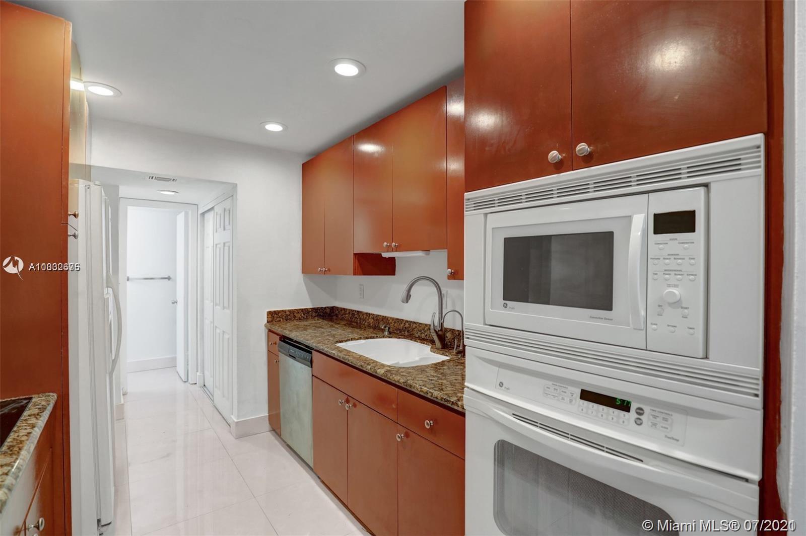 a hallway with granite countertop stainless steel appliances white cabinets and a wooden floor
