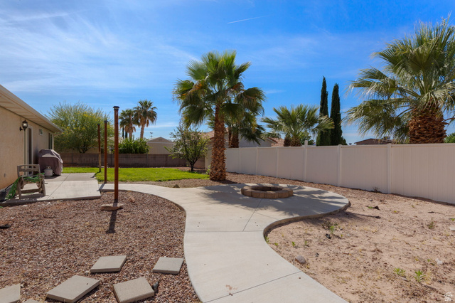 664 East Springhill Drive Washington, UT 84780 - Photo 21 of 21 Expansive backyard featuring a curved concrete pathway, stone fire pit, and mature palm trees