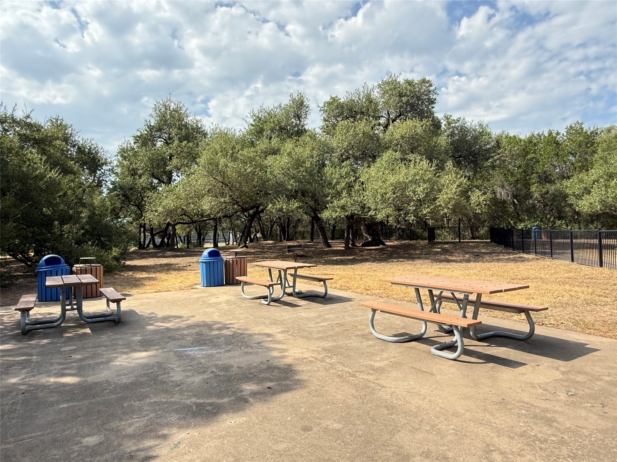 7826 Wheel Rim Circle Austin, TX 78749 - Photo 29 of 38 Mature shade trees frame a concrete picnic area alongside a fenced perimeter.