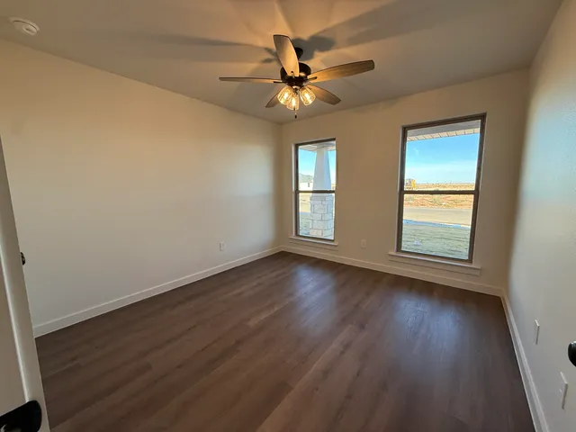 an empty room with wooden floor fan and windows