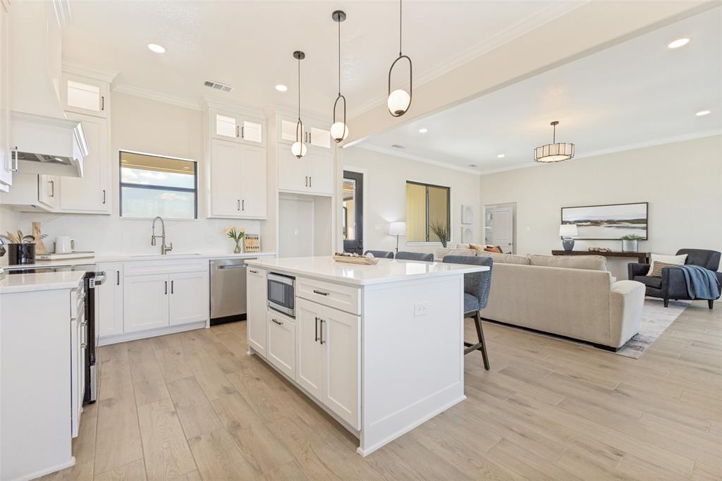 3150 Crisp Road Ennis, TX 75119 - Photo 7 of 30 Open-concept kitchen featuring an island with built-in microwave, white cabinetry, integrated stainless steel appliances, and wood-finish flooring