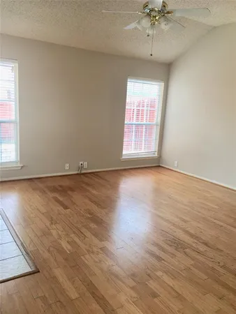 an empty room with wooden floor chandelier fan and windows