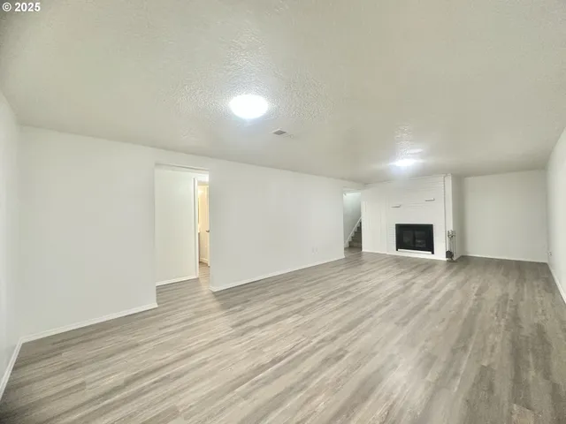 a view of an empty room with wooden floor and fireplace
