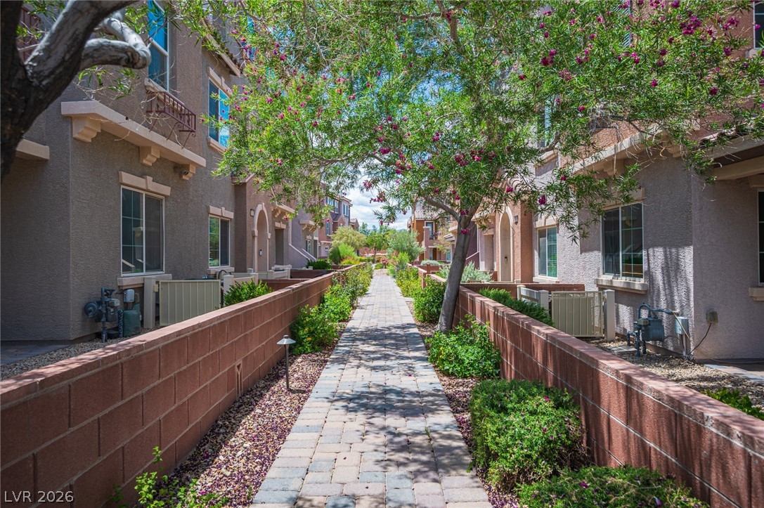 9916 Sable Point Street Las Vegas, NV 89178 - Photo 4 of 73 A charming brick paved walkway meanders through a residential area, framed by low walls and vibrant green landscaping.